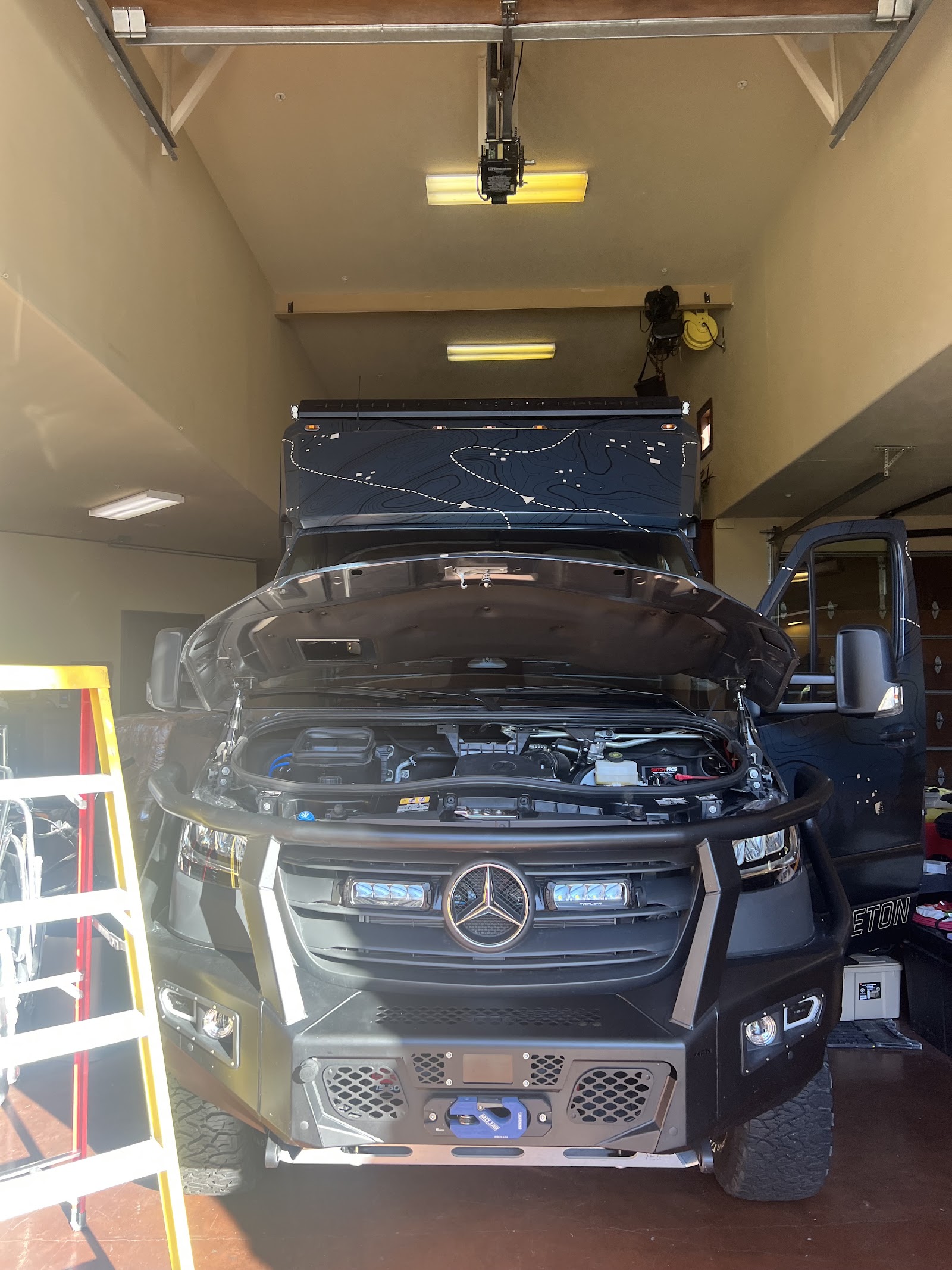 Mercedes overland truck with hood open being serviced in a garage