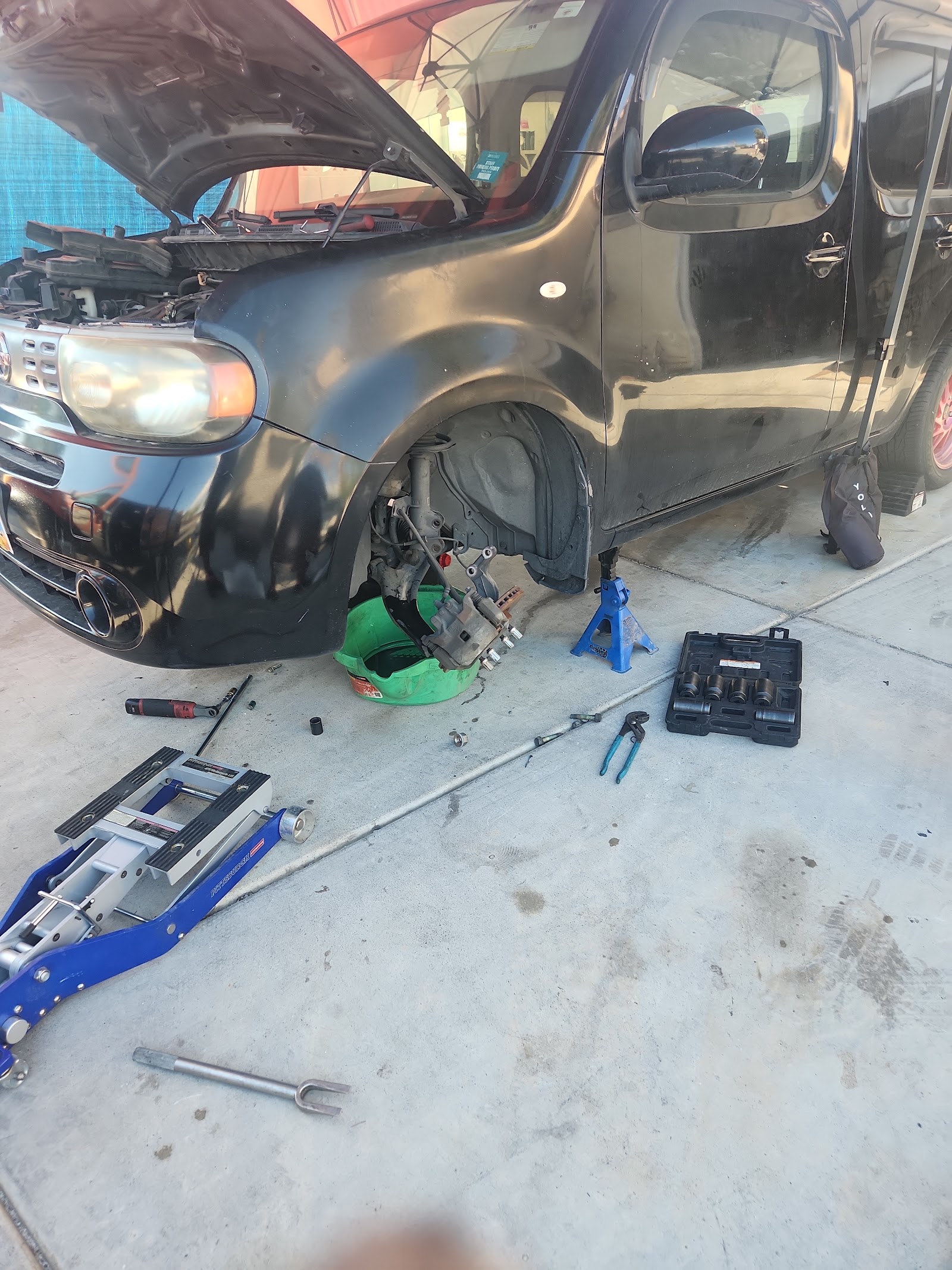 Black Nissan Cube on jack stands with brake components and tools during a repair
